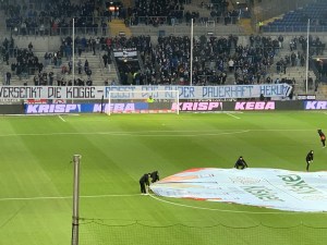 Stadiontribühne in Bielefeld, auf einer Zaunfahne steht: Versenkt die Kogge, Reißt das Ruder dauerhaft herum