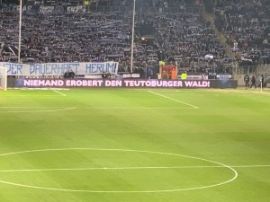 Stadiontribüne in Bielefeld, davor elektronische Werbebande mit der Aufschrift: Niemand erobert den Teutoburger Wald