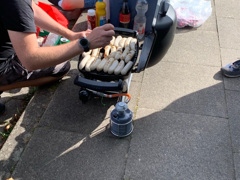 Auf einem Gasgrill werden Bratwürste vorbereitet.