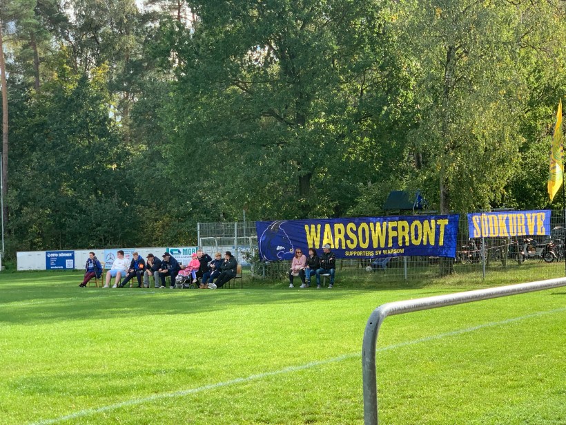 Rechte Bildhälfte: Zaunfahnen, Gelbe Schrift auf blauem Grund: