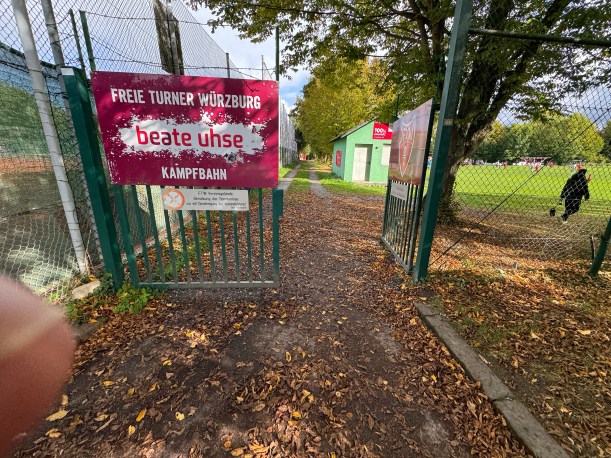Ein rotes Schild mit der Aufschrift Freie Turner Würzburg beate uhse Kampfbahn an einem grünen Metalltor